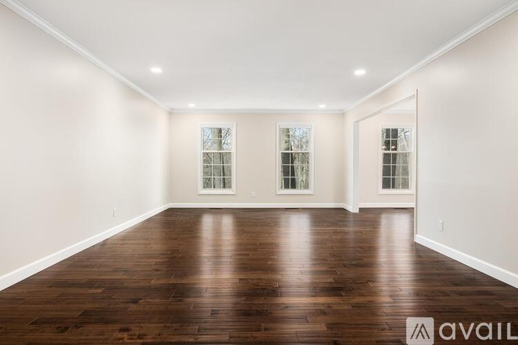 A spacious room with wooden floors and three windows.