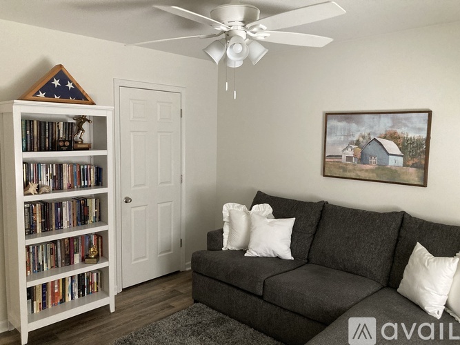 A living room with a grey couch, a bookshelf, and a painting on the wall.