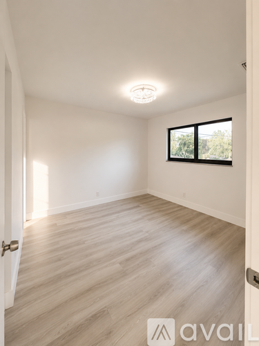 A room with wooden flooring and a window with a view of trees.