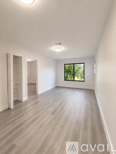 A spacious room with wooden flooring and a window overlooking greenery.