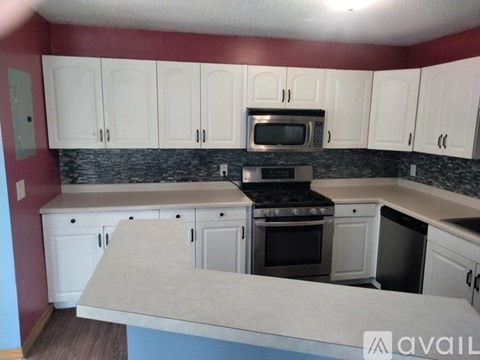 A kitchen with white cabinets and a maroon wall.