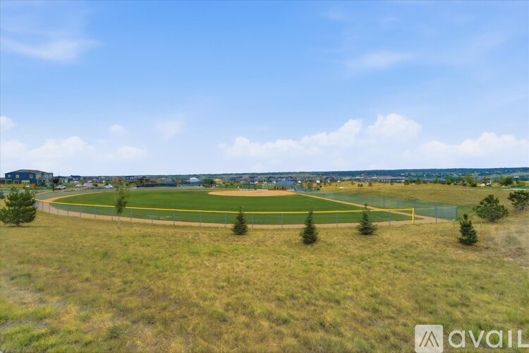 A field with a fence and trees in the distance under a blue sky.