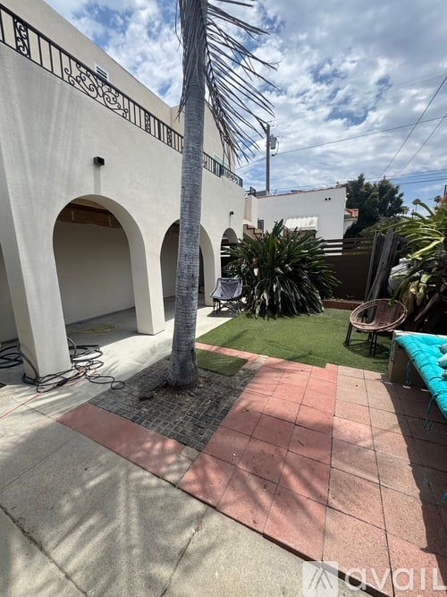 A palm tree stands in front of a white building with arches.