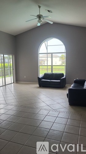 A living room with a black couch and a fan.