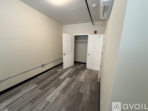 A room with a grey floor and white walls has a doorway leading to another room.