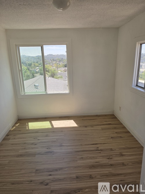 A room with wooden floors and a window overlooking a residential area.
