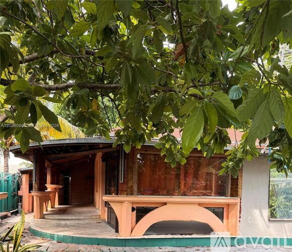 A house with a brown roof and a green fence is surrounded by trees.
