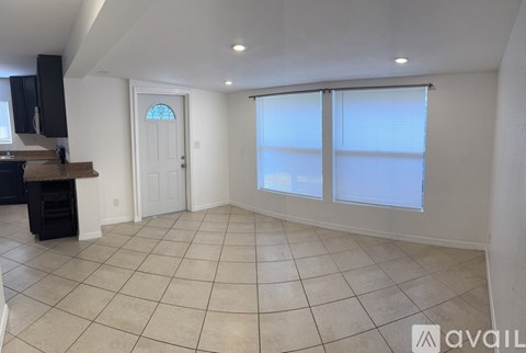 A spacious room with tiled flooring and a large window with blinds.