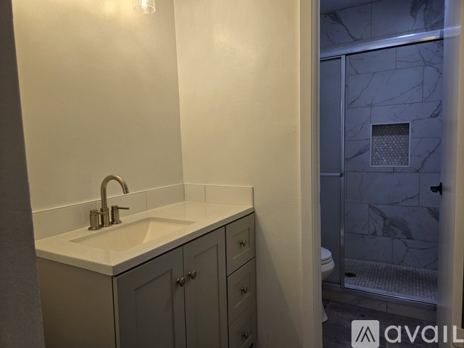 A bathroom with a sink, grey cabinets and a marble tiled shower.