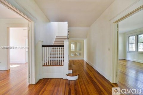A room with wooden floors and a staircase in the background.