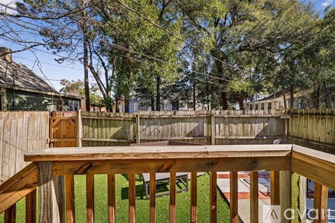 A wooden deck overlooks a backyard with a fence and trees.