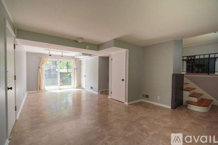 A spacious room with a staircase and a window with curtains.
