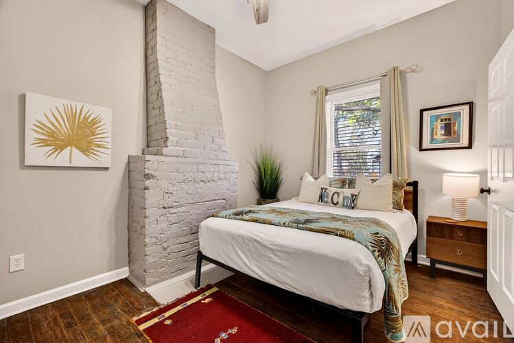A bedroom with a white brick chimney and a bed with a white comforter.
