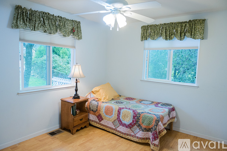 A bedroom with a bed, a nightstand, and a window with a view of trees.