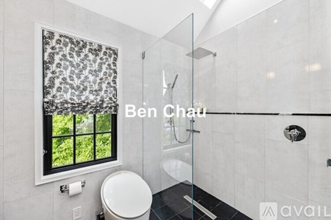 A bathroom with a toilet, a window with a view of trees, and a glass shower stall.