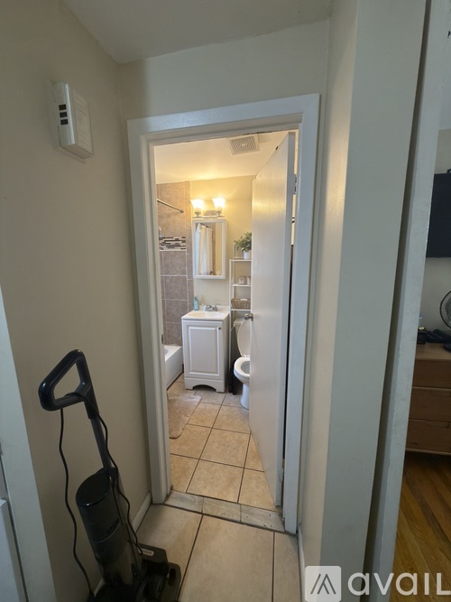 A vacuum cleaner is on the floor in a narrow hallway leading to a bathroom.