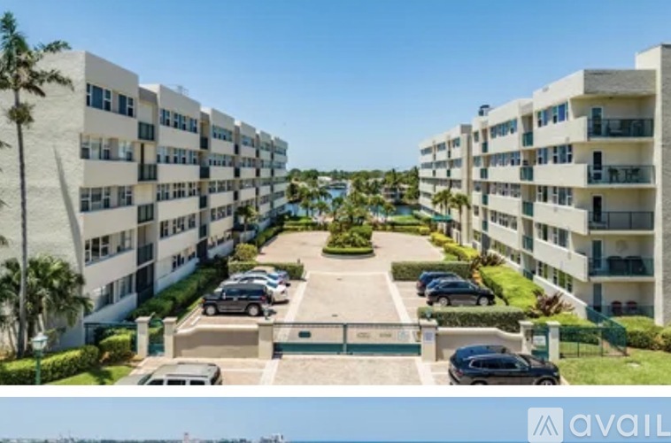 A row of white apartment buildings with cars parked in front.