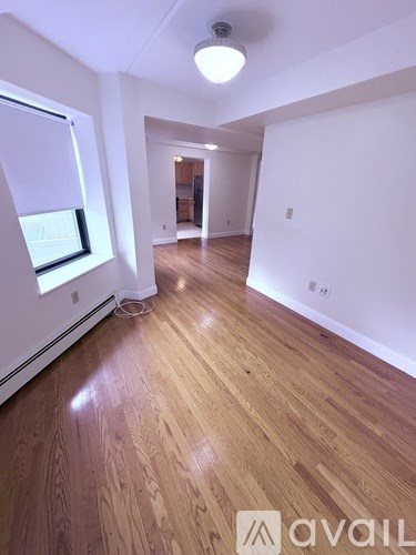 A room with wooden flooring and a window on the left side.
