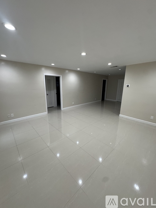 A spacious room with white tiled flooring and recessed lighting.