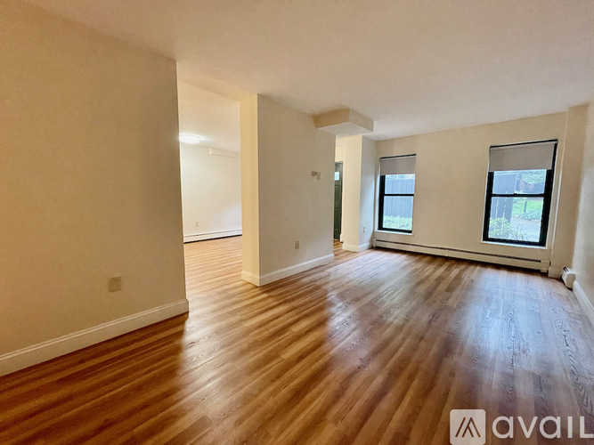A spacious room with wooden flooring and two windows.