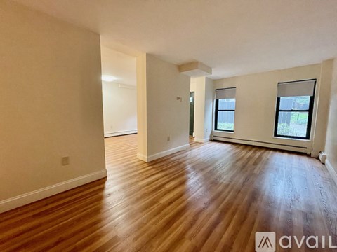 A spacious room with wooden flooring and two windows.