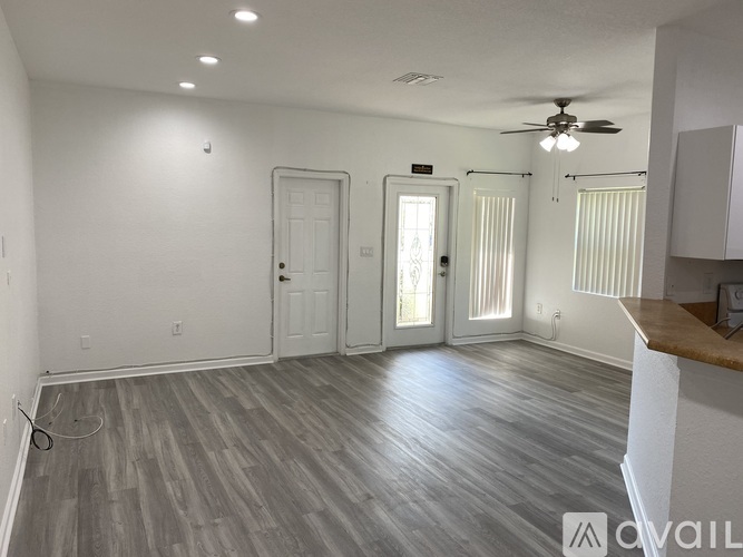 A spacious room with a ceiling fan and lighting, featuring a wooden floor and white walls.