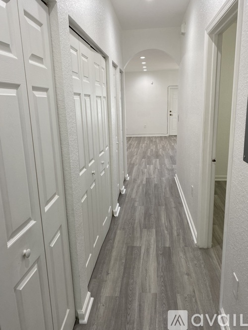 A long hallway with white doors and grey wood flooring.