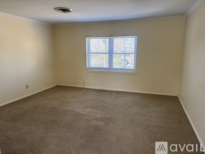 A room with a carpeted floor, a window with blinds, and a ceiling light fixture.