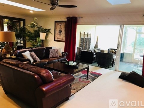 A living room with a brown leather couch and a ceiling fan.