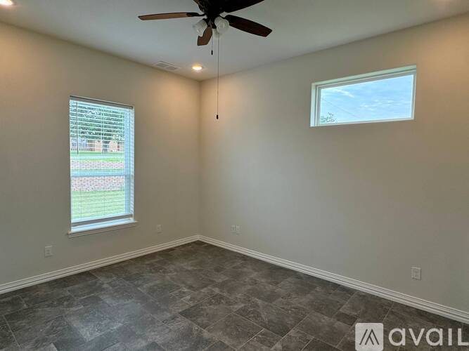 A room with a ceiling fan and a window with a view of a lawn and trees.