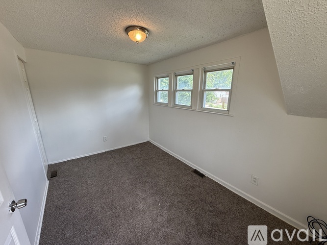 A room with a carpeted floor and a window with a view of trees.