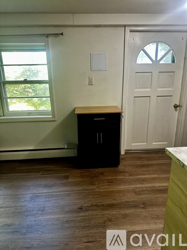 A room with a white door, a window with blinds, and a wooden cabinet.