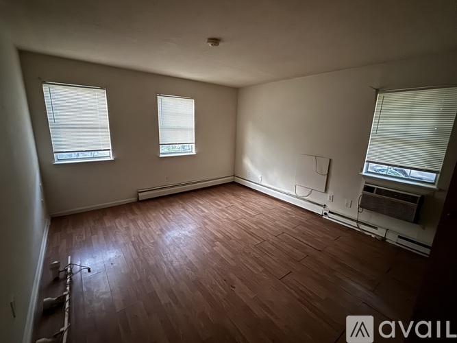 A room with wooden flooring and three windows.