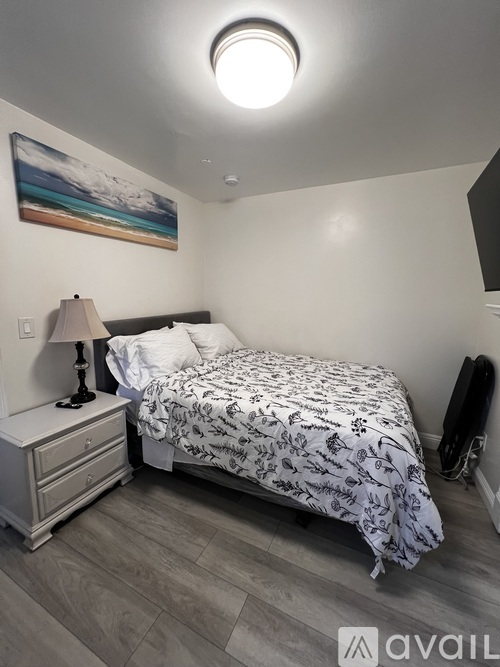 A bedroom with a bed, nightstand, and a painting on the wall.