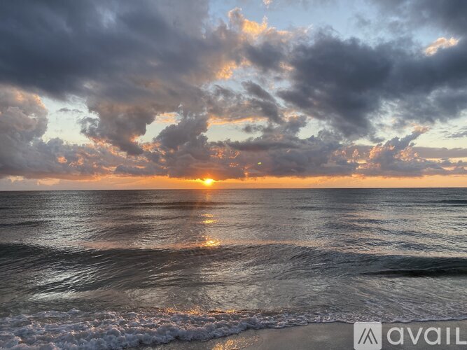 The sun is setting over the ocean with waves crashing onto the shore.