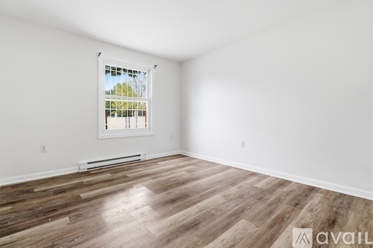 A room with wooden flooring and a window showing a view of trees outside.