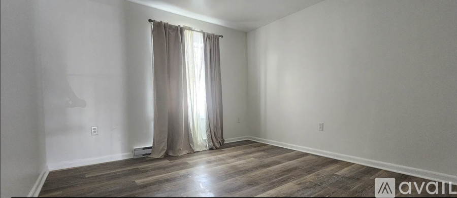 A room with a window covered by curtains and wooden flooring.