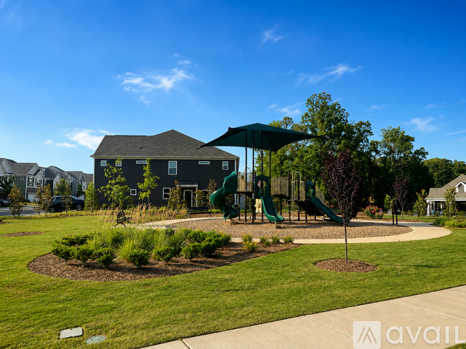 A playground with a green slide and a brown tree is in front of a house.