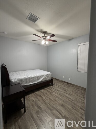 A bedroom with a bed, a ceiling fan, and a wooden floor.