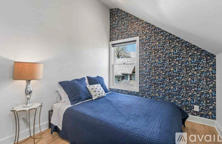 A bedroom with a blue bedspread and a wallpapered wall with a picture of a house.