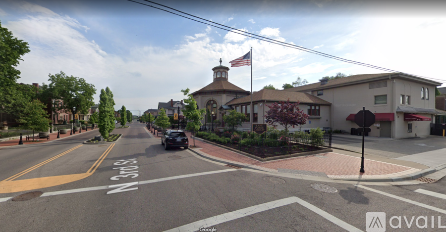 A street view with a car driving on the road and a building with a flag on top.