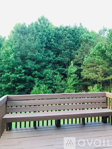 A wooden bench sits on a deck with trees in the background.