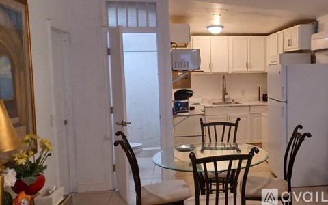 A kitchen with a table and chairs in the foreground and a refrigerator, sink, and cabinets in the background.