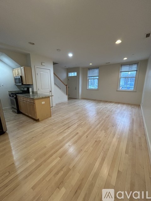 A room with wooden flooring and a kitchen area with a microwave and refrigerator.