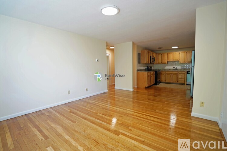 A room with wooden flooring and a kitchen in the background.