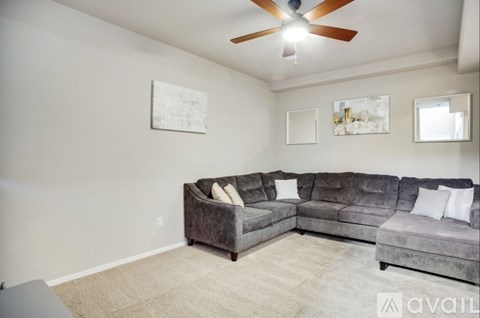 A living room with a grey couch and a fan on the ceiling.