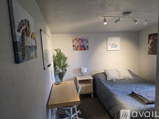 A bedroom with a bed, desk, and a plant.