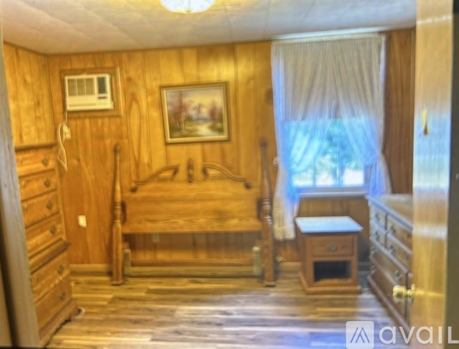 A wooden bedroom with a bed, dresser, and window.