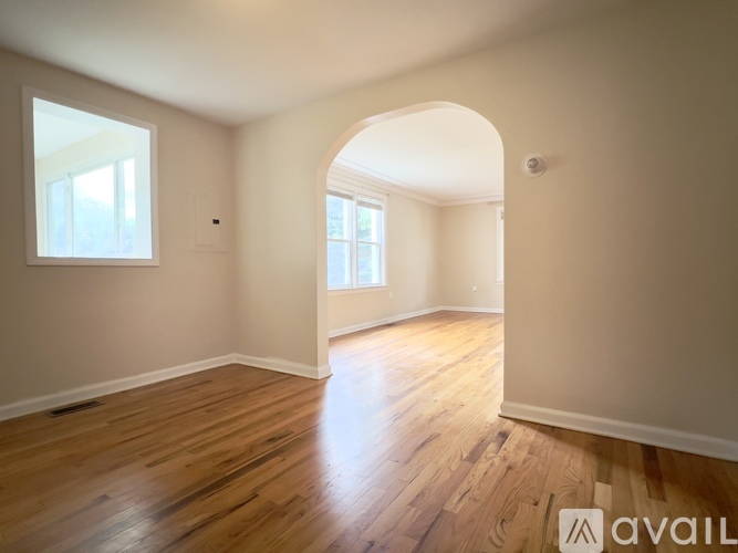 A spacious room with wooden flooring and a large archway leading to another room.
