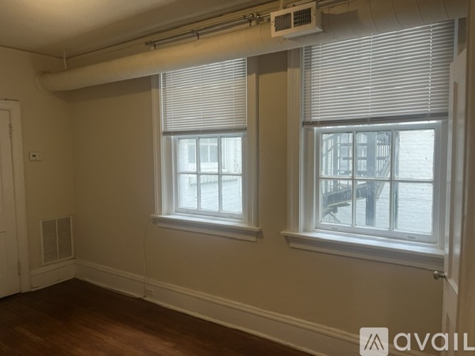 Two windows with blinds in a room with wooden floors and white walls.